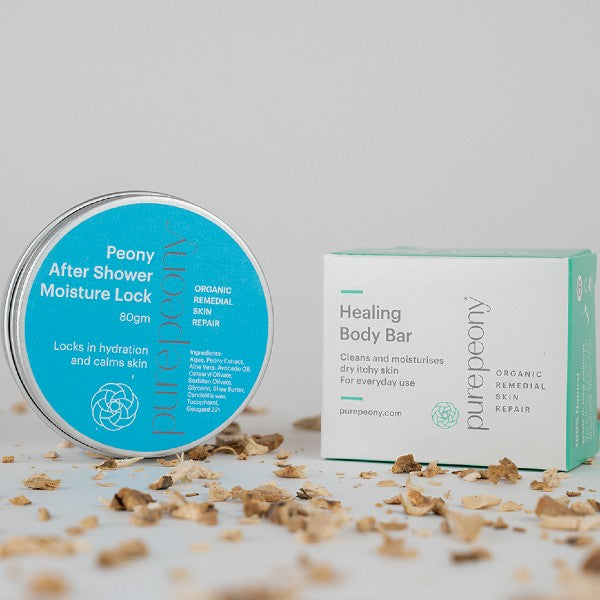 80gm tin of After Shower Lock next to Box of Healing Body Bar on a bed of scattered dried peony root