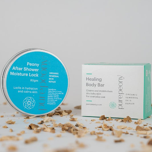 80gm tin of After Shower Lock next to Box of Healing Body Bar on a bed of scattered dried peony root