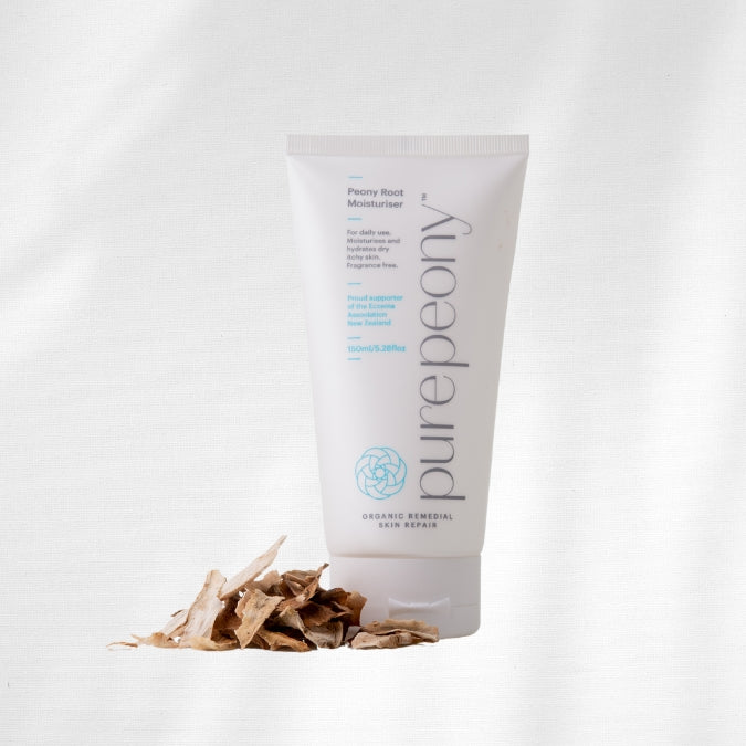 Tube of purepeony moisturiser with dried peony roots on a white background
